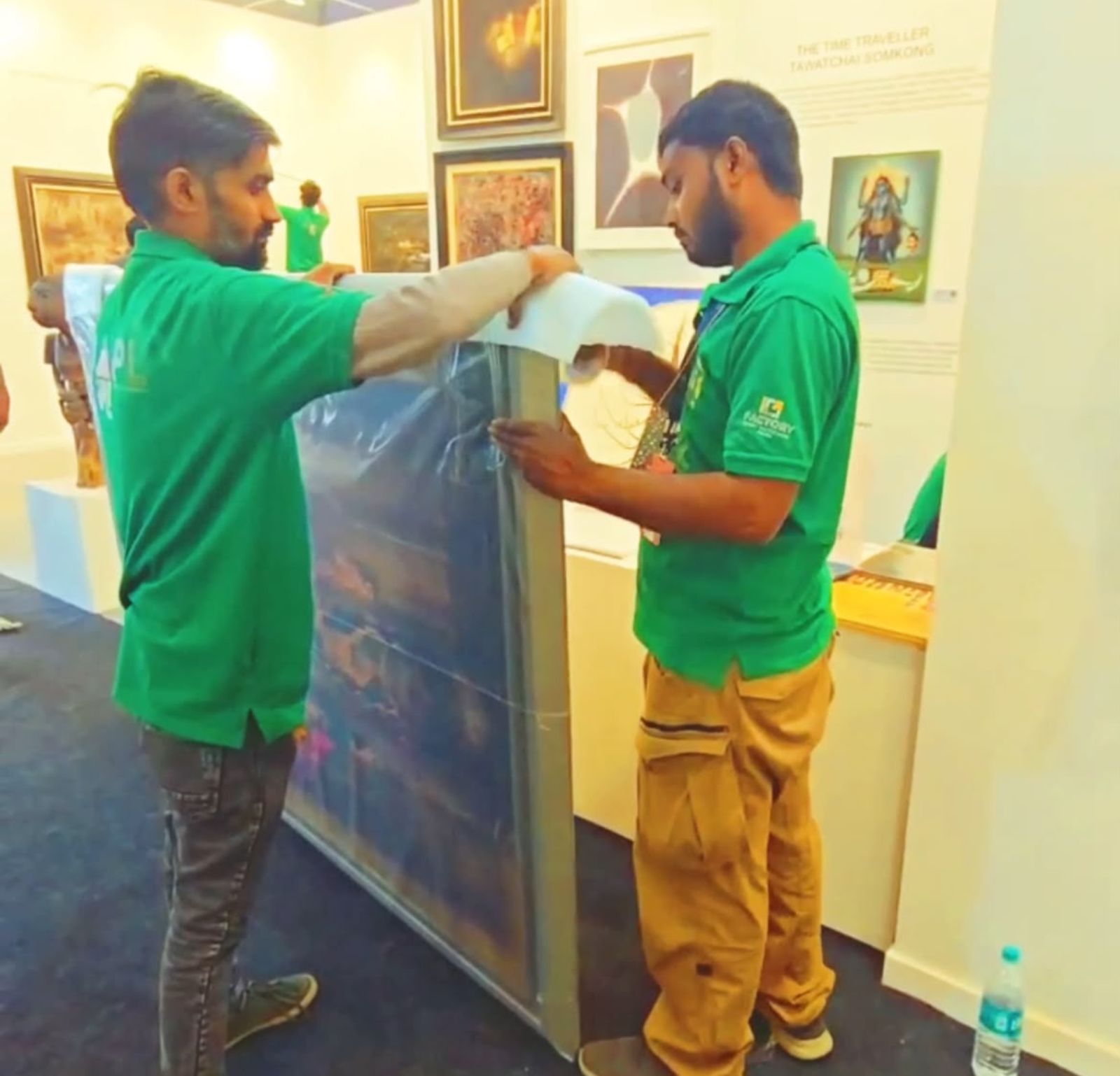 Two UAPL handlers wrapping a large framed painting in protective film at a fair booth