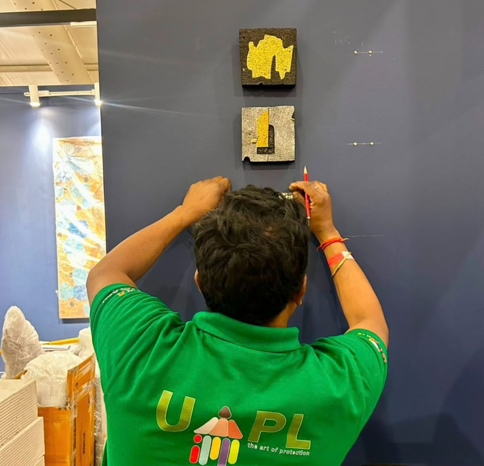 A UAPL handler marking hanging positions in pencil beside two small textured artworks on a blue wall